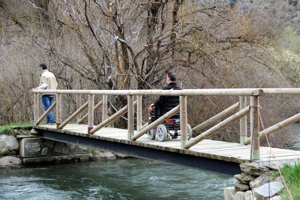 Dos homes passant per un pont sobre el riu Noguera Pallaresa, en un itinerari adaptat per persones amb cadires de rodes. Imatge del 24 d'abril del 2018. (horitzontal)