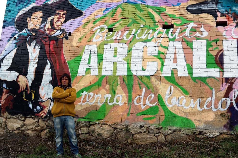 Xavi Pedemonte davant del mural que dona la benvinguda al poble d'Arcal√≠s i est√† dedicat als bandolers. imate del 26 de novembre del 2018. (horitzontal)