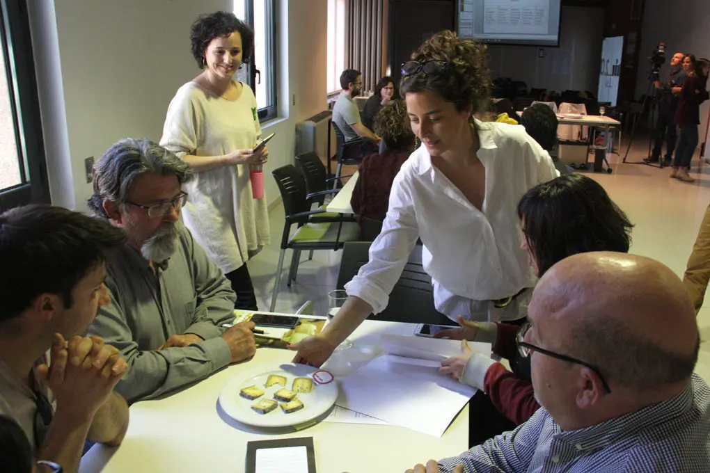 Pla general d'un grup de participants de la jornada t&radic;&reg;cnica sobre el formatge artes&radic;&dagger; del Pirineu a la cuina, a punt de valorar un dels formatges que els porta la directora cient&radic;&ne;fica de la Fundaci&radic;&ge; Al&radic;&ne;cia, Elena Roure, el 20 de mar&radic;&szlig; de 2019 (Horitzontal).
