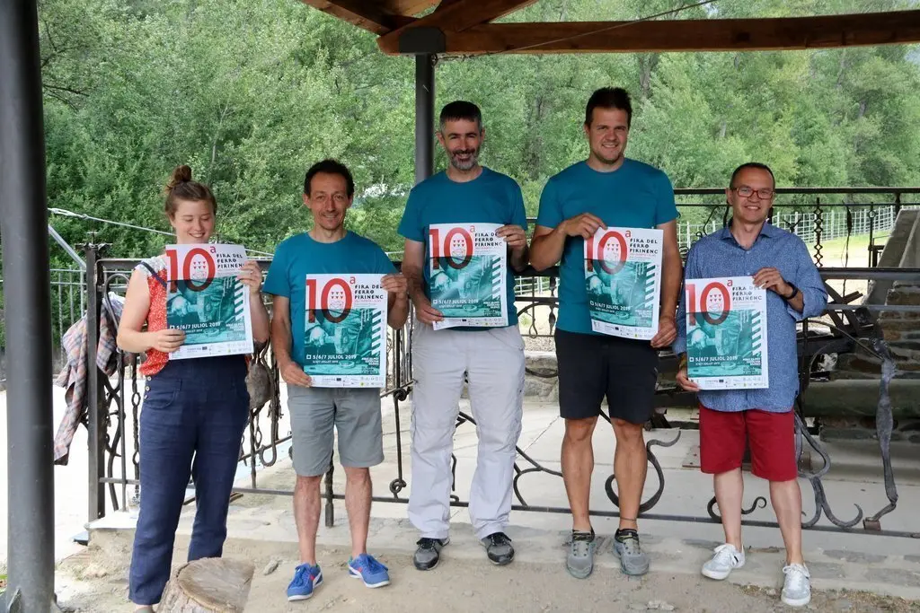 Imatge dels organitzadors de la Fira del Ferro d'Alins, al Pallars Sobir&agrave;, amb el cartell promocional. Imatge del 4 de juliol del 2018. (horitzontal)