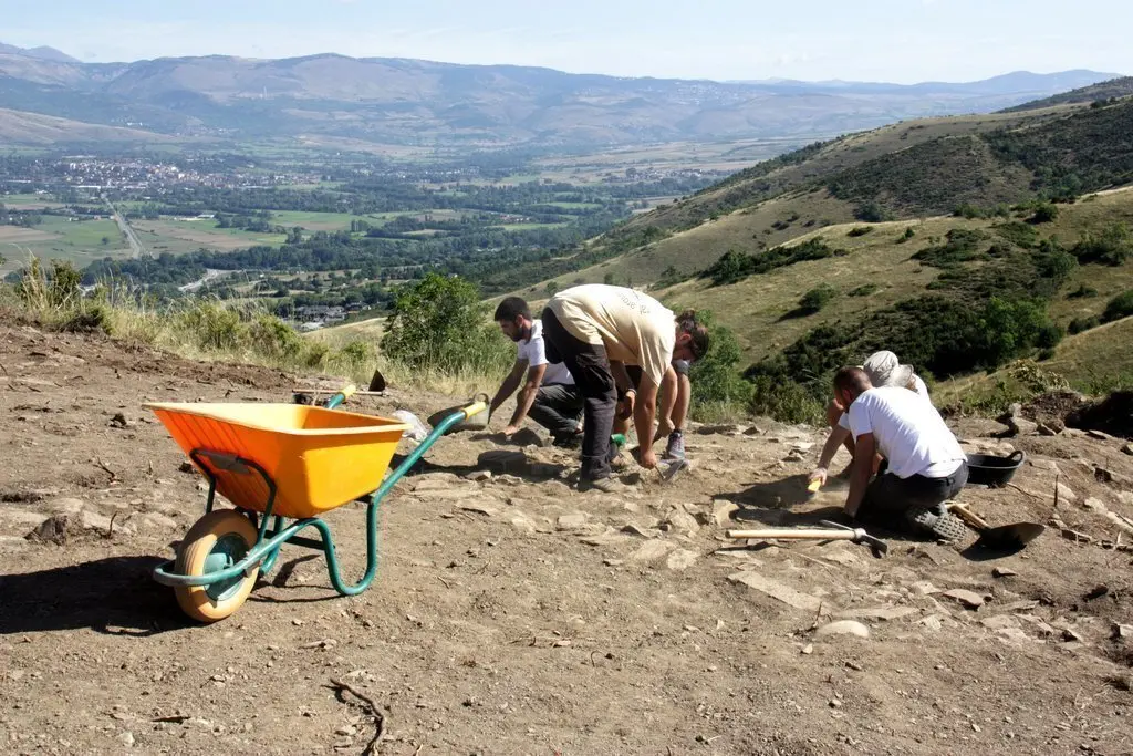 Pla general d'un grup d'arque&ograve;legs excavant el jaciment del Serrat del Castellar, a Fontanals de Cerdanya, on es veu part de la vall que hi queda a sota del tur&oacute;. Imatge del 29 d'agost de 2019 (Horitzontal).