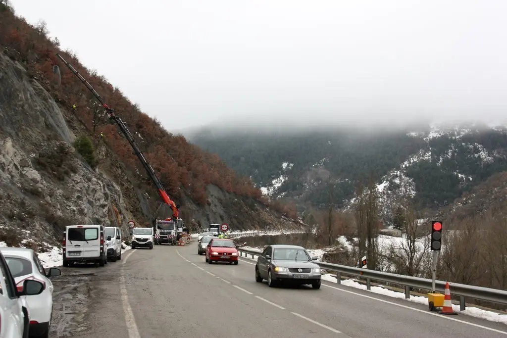Pla general de diversos vehicles circulant en pas alternatiu regulat amb sem&agrave;fors a l'N-260 al Pont de Bar (Alt Urgell) i una grua que porta malla al punt on aquest dijous s'ha produ&iuml;t una esllavissada. Imatge del 24 de gener de 2020 (Horitzontal).