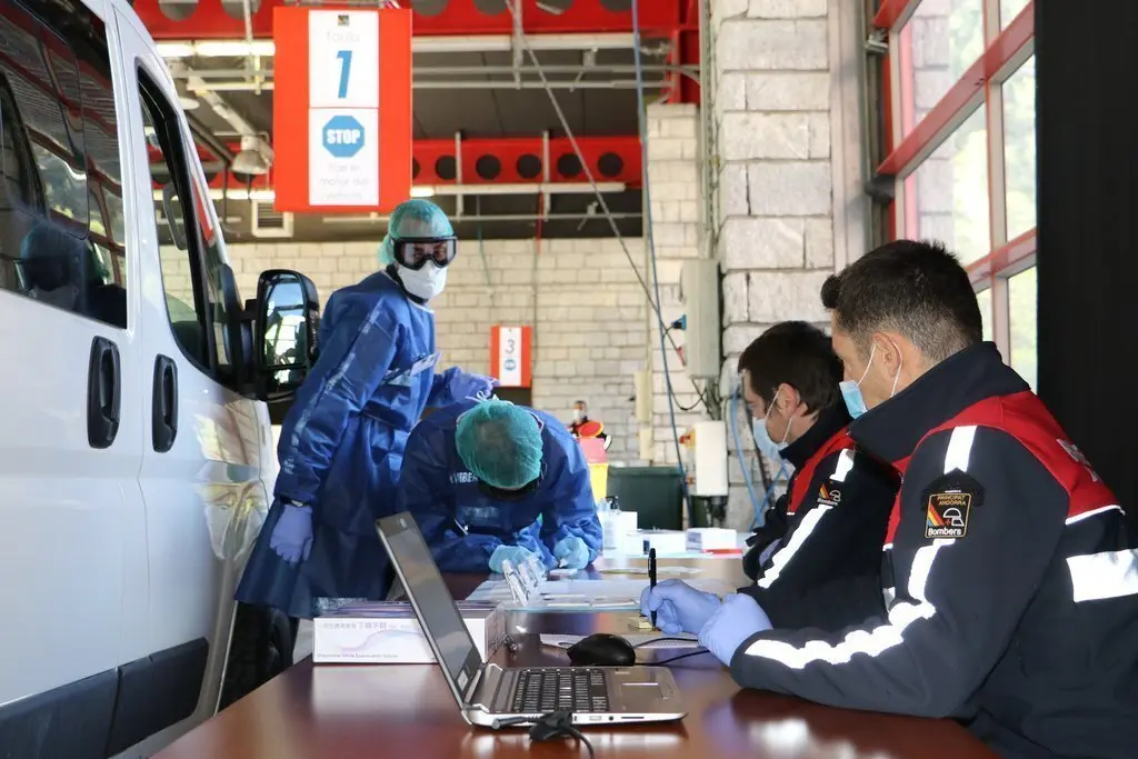 Pla obert de dos bombers en un dels punts habilitats dins la caserna per fer els tests d'anticossos de la covid-19 on es veu un vehicle al costat. Imatge de l'Ag&egrave;ncia de Not&iacute;cies Andorrana (ANA) del 29 d'abril de 2020 (Horitzontal).
