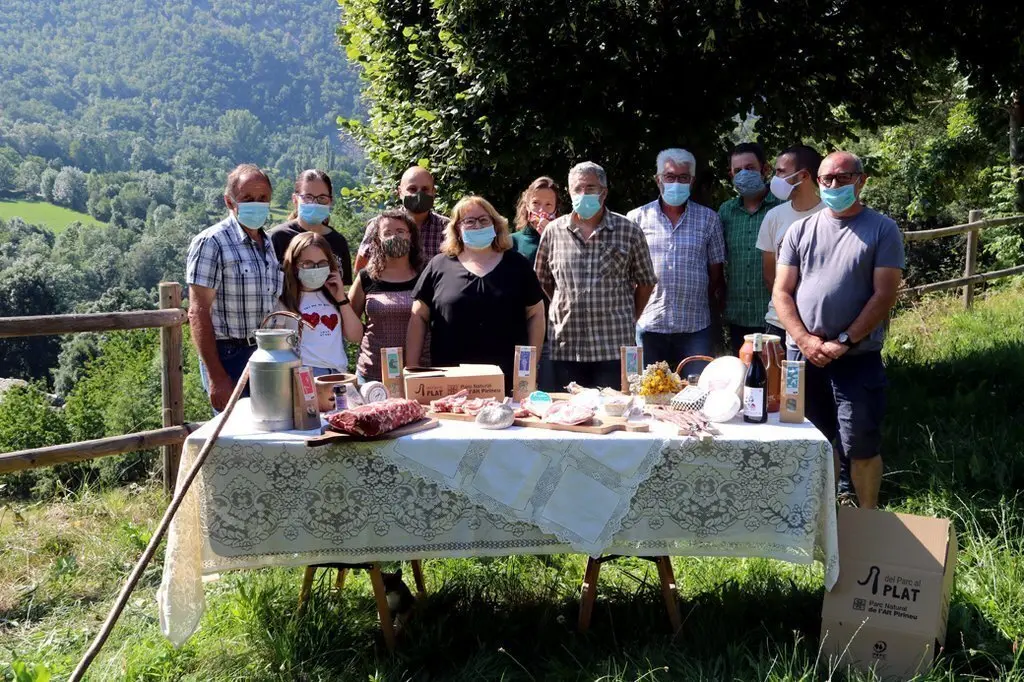 Pla obert on es veuen els productors de l'entorn del Parc Natural de l'Alt Pirineu que s'han unit en una associaci&radic;&ge; darrere una taula on hi han alguns dels productes que elaboren. Imatge del 30 de juny de 2020 (Horitzontal).