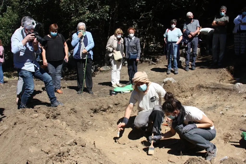 Pla obert de dos arque&ograve;legs analitzant el qu&egrave; han trobat en l'excavaci&oacute; d'una fossa de la Guerra Civil a Sorpe, a l'Alt &Agrave;neu (Pallars Sobir&agrave;), i familiars de les v&iacute;ctimes que hi hauria enterrades mirant-ho darrere, el 2 de setembre de 2020 (Horitzontal).