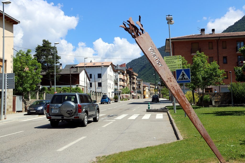 Pla general de l'entrada al poble de Vilaller (Alta Ribagorça) amb una escultura d'una falla en primer terme. Imatge del 30 de maig del 2020. (horitzontal)