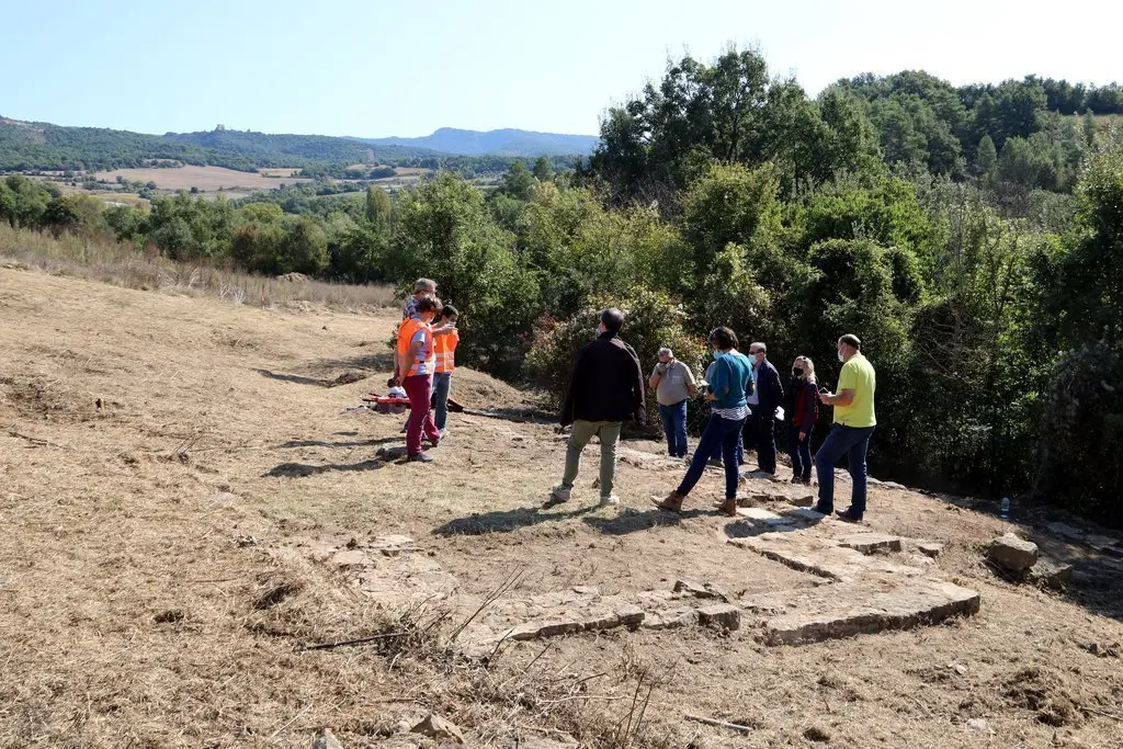 En primer pla restes de les parets de la casa residencial de la vil&middot;la romana de Llor&iacute;s i al fons els arque&ograve;legs explicant el jaciment el dia 30 de setembre del 2020. (horitzontal)