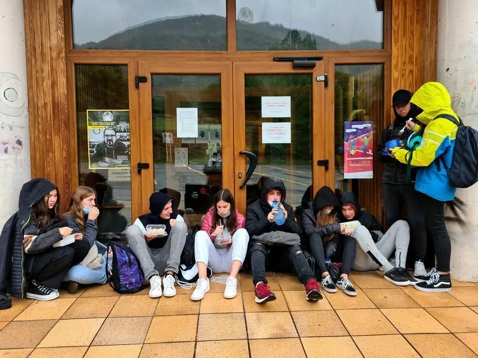 Pla general d'un grup de joves dinant amb carmanyola a la porta de l'Arxiu Comarcal del Pallars Sobir&agrave; on es resguardaven de la pluja el 2 d'octubre del 2020. (horitzontal)