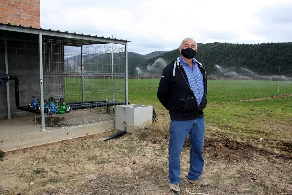 Pla general del president de la comunitat de regants de Peramola-Bassella, Joan Puig, a la seva finca, on es veu al fons la canonada i el reg per aspersi&oacute; per on surt l'aigua. Imatge del 26 de novembre de 2020 (Horitzontal).