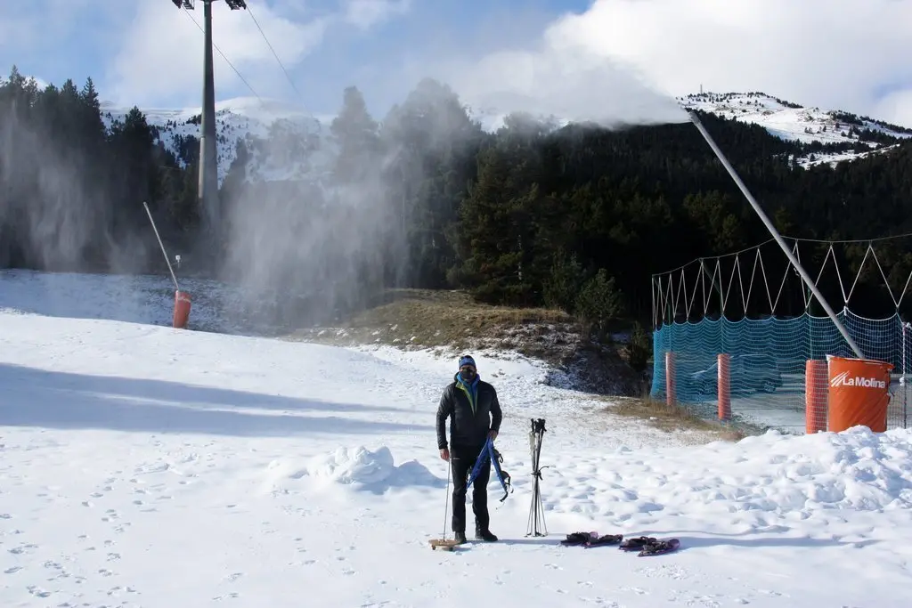 Pla general del director d'Altitud Extrem, Xavi Fanlo, preparant les raquetes per una excursi&oacute; guiada a la base de l'estaci&oacute; de La Molina (Cerdanya) i on es veu un can&oacute; produint neu. Imatge del 2 de desembre de 2020 (Horitzontal).
