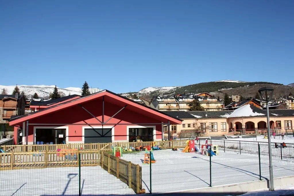 Pla obert on es veu part de l'edifici de la nova Escola Jaume I de Ll&iacute;via (Cerdanya) i la Llar d'infants Els Esquirolets amb alguns alumnes jugant amb la neu al pati i l'antiga escola al fons. Imatge de l'11 de gener de 2021 (Horitzontal).