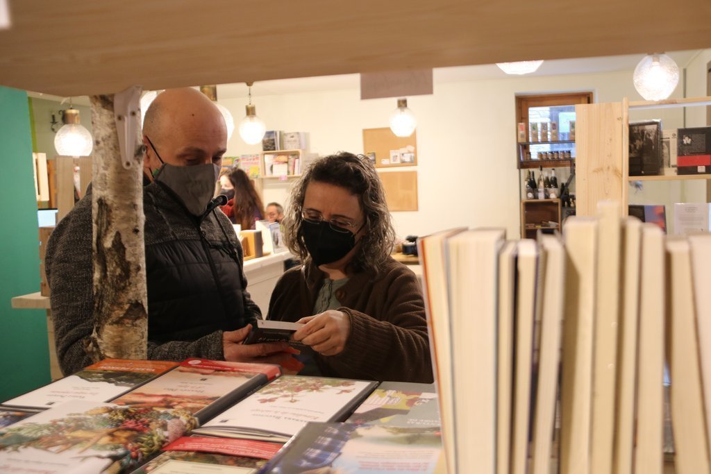 Pla mig de dos clients a la llibreria NaturaLlibres d'Alins fullejant algun llibre el 25 de gener del 2021. (horitzontal)