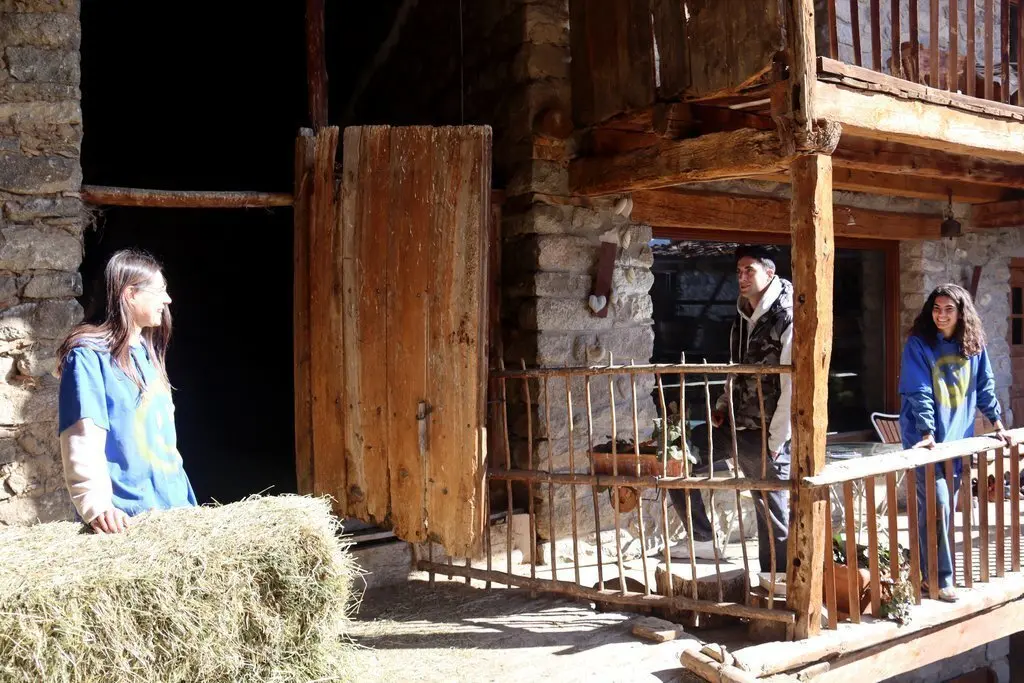 Pla obert de la Maragda Farr&agrave;s, a l'esquerra, parlant amb dos amics a la casa de M&uacute;sser, a Lles de Cerdanya, que s'est&agrave; rehabilitant per acollir el Taller d'Entorns dedicat a la creaci&oacute; art&iacute;stica. Imatge del 16 de mar&ccedil; de 2021 (Horitzontal).