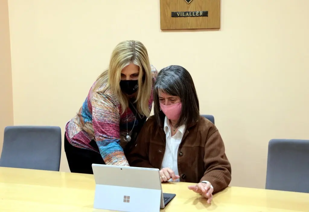 Pla mig de l'alcaldessa de Vilaller, Maria Jos&eacute; Erta, amb una dona que est&agrave; teletreballant a la sala de plens. Imatge de l'11 de maig del 2021. (horitzontal)