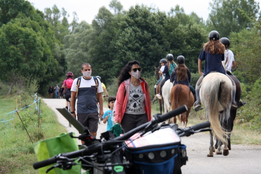 Pla obert on es veu un grup de persones passejant i altres a sobre d'un cavall passant per un camí que discorre a l'entorn del riu Segre a Isòvol i part d'unes bicicletes desenfocades en primer terme. Imatge del 18 d'agost de 2020 (Horitzontal).
