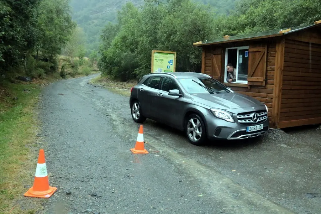 Pla obert de la caseta i del vigilant que controla l'acc&eacute;s als aparcaments que donen acc&eacute;s a la Pica d'Estats i un vehicle sortint de la zona, el 31 de juliol del 2021. (Horitzontal)