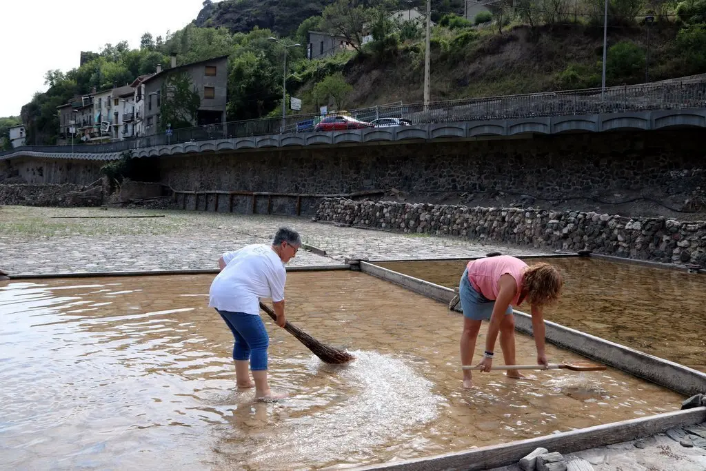 Pla general de dos persones trencant la crosta de la sal a una de les salines en funcionament de Gerri de la Sal. Imatge del 3 d'agost del 2021. (Horitzontal)