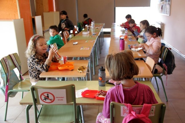 Pla general d'un grup de nens del casal d'estiu de Ger asseguts en cadires i on es veuen altres de buides amb un cartell que indica que no poden seure per mantenir la distància de seguretat. Imatge del 8 de juny de 2020 (Horitzontal).