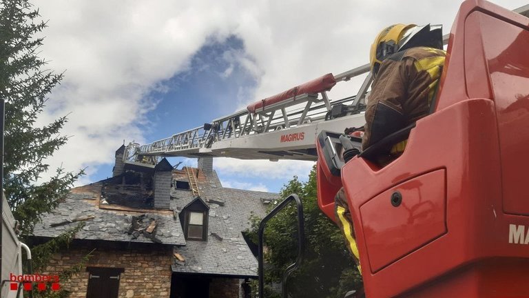 Pla detall dels Bombers treballant en l'incendi de la teulada d'un habitatge d'apartaments prop de l'estació d'esquí d'Espot. Imatge del 26 de juliol de 2021. (Horitzontal)