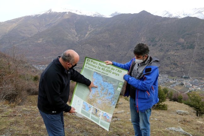 Pla general de dos persones mostrant el pòster sobre la glacera de la Noguera Pallaresa que ha editat el Parc Natural de l'Alt Pirineu. Imatge del 5 de febrer del 2021. (horitzontal)