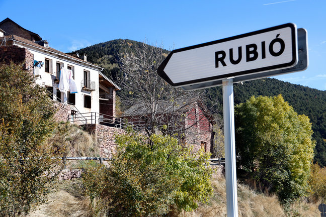 Pla de detall del r√®tol del poble de Rubi√≥, amb cases del nucli al fons. Imatge del 29 d'octubre del 2021. (Horitzontal)