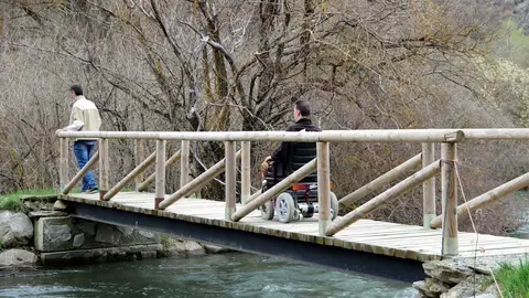 Dos homes passant per un pont sobre el riu Noguera Pallaresa, en un itinerari adaptat per persones amb cadires de rodes. Imatge del 24 d'abril del 2018. (horitzontal)