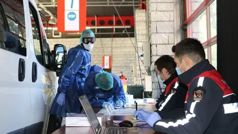 Pla obert de dos bombers en un dels punts habilitats dins la caserna per fer els tests d'anticossos de la covid-19 on es veu un vehicle al costat. Imatge de l'Ag&egrave;ncia de Not&iacute;cies Andorrana (ANA) del 29 d'abril de 2020 (Horitzontal).
