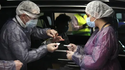 Pla mitj&agrave; de dos membres de l'operativa per a la realitzaci&oacute; de tests massius a la poblaci&oacute; d'Andorra, a punt de fer una de les proves amb una petita extracci&oacute; de sang d'una persona que est&agrave; a l'interior d'un vehicle, el 4 de maig de 2020 (Horitzontal).