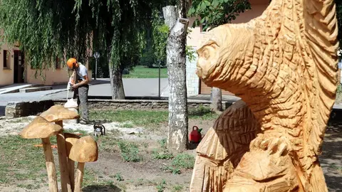 Primer pla d'una escultura de fusta i al fons l'artesa treballant amb motoserra el 27 de juliol del 2020. (horitzontal)