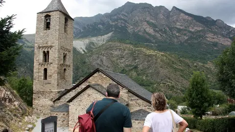 Pla obert de l'esgl&eacute;sia de Sant Joan de Bo&iacute;, a la Vall de Bo&iacute; (Alta Ribagor&ccedil;a), on es veu en primer terme dos turistes accedint-hi al seu entorn i un cartell on hi ha els codis QR per comprar les entrades per Internet, el 14 d'agost de 2020 (Horitzontal).