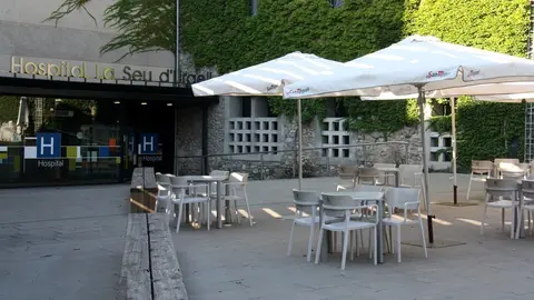 Pla obert on es veu l'exterior del Sant Hospital de la Seu d'Urgell i on hi ha diverses taules d'una terrassa d'un bar col&middot;locades en primer terme. Imatge del 20 d'agost de 2020 (Horitzontal).