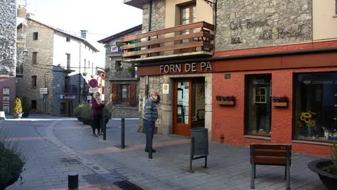 Pla obert d'un carrer de Bellver de Cerdanya on hi ha diversos comer&ccedil;os i on es veu dues persones esperant per entrar al forn de pa en el primer dia de confinament municipal de cap de setmana. Imatge del 30 d'octubre de 2020 (Horitzontal).