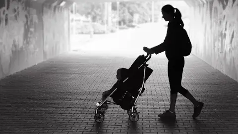 Single mother walking in city tunnel with baby in stroller.