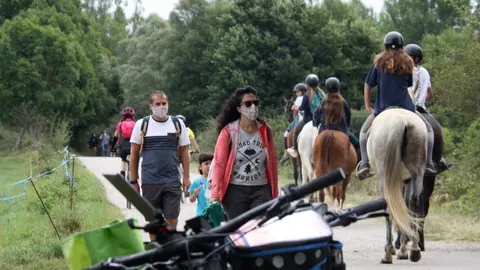 Pla obert on es veu un grup de persones passejant i altres a sobre d'un cavall passant per un cam&iacute; que discorre a l'entorn del riu Segre a Is&ograve;vol i part d'unes bicicletes desenfocades en primer terme. Imatge del 18 d'agost de 2020 (Horitzontal).