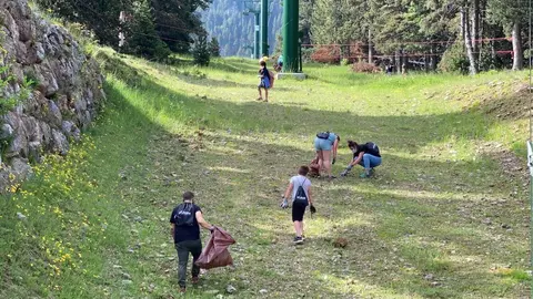 Pla obert d'un grup d'alumnes de l'Escola Bac de Cerdanya d'Alp recollint residus sota un remuntador de l'estaci&oacute; de La Molina. Imatge del 16 de juny de 2021. (Horitzontal)