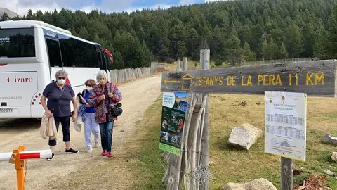 Pla obert on es veuen tres persones al costat d'un dels busos llan&ccedil;adora que cobreix el trajecte entre l'aparcament del Refugi Cap del Rec, a la base de l'estaci&oacute; de n&ograve;rdic de Lles, i la font de Pollineres. Imatge de l'1 de setembre de 2021. (Horitzontal)