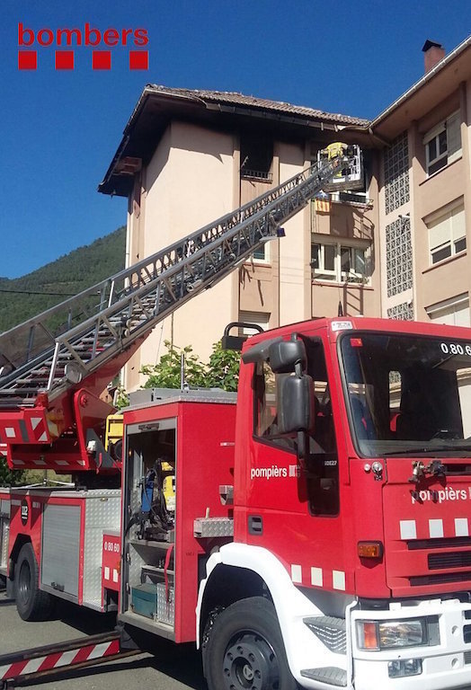 Imatge general de l'edifici de Vilaller on ha cremat el tercer pis en un incendi, amb vehicles de bombers i una grua en primer terme, aquest 20 d'agost del 2017 (vertical)