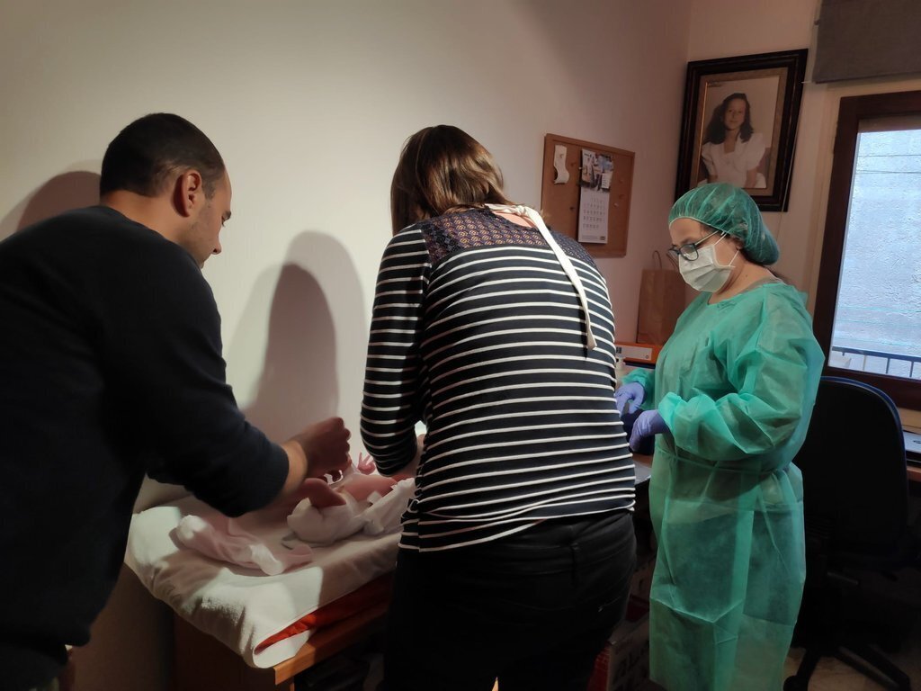 Pla americà on es veu una professional de l'equip de Pediatria dels Pirineus visitant un nadó a domicili, amb els seus pares al costat. Imatge facilitada per Pediatria dels Pirineus el 12 d'abril de 2020 (Horitzontal).