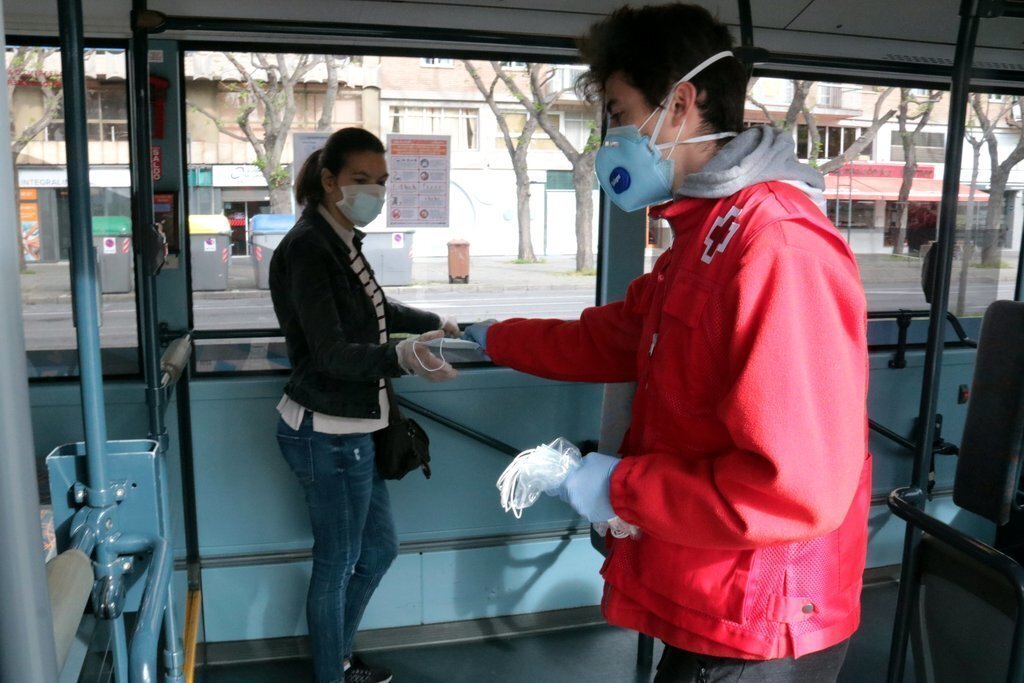 Un voluntari de Creu Roja lliurant una mascareta a una usuària d'un autobús a Lleida, el 14 d'abril del 2020. (Horitzontal)