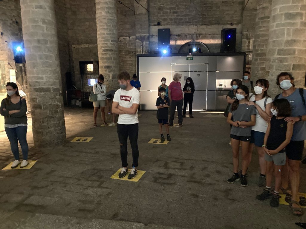 Pla obert de l'interior de l'església de Sant Climent de Taüll, a la Vall de Boí (Alta Ribagorça),on es veu a una vintena de persones col·locades per veure el videomapatge de les pintures. Imatge del 14 d'agost de 2020 (Horitzontal).