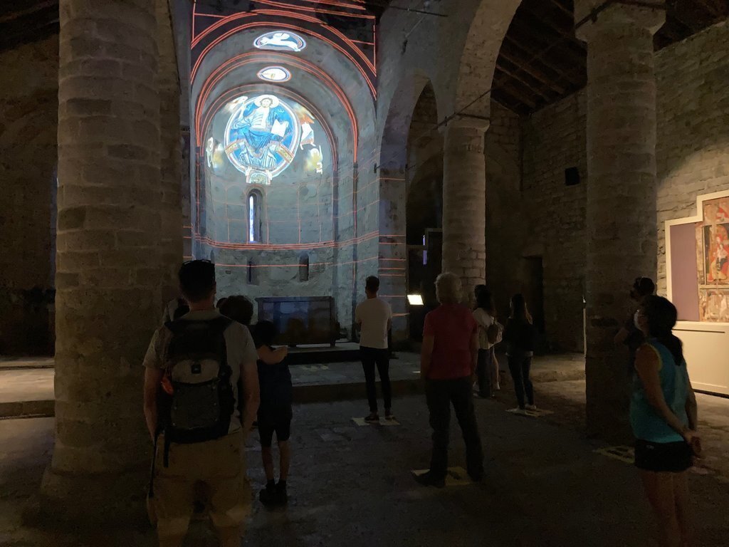 Pla general de l'interior de l'església de Sant Climent de Taüll, a la Vall de Boí (Alta Ribagorça), amb gairebé una vintena de persones veient el videomapatge de les pintures. Imatge del 14 d'agost de 2020 (Horitzontal).