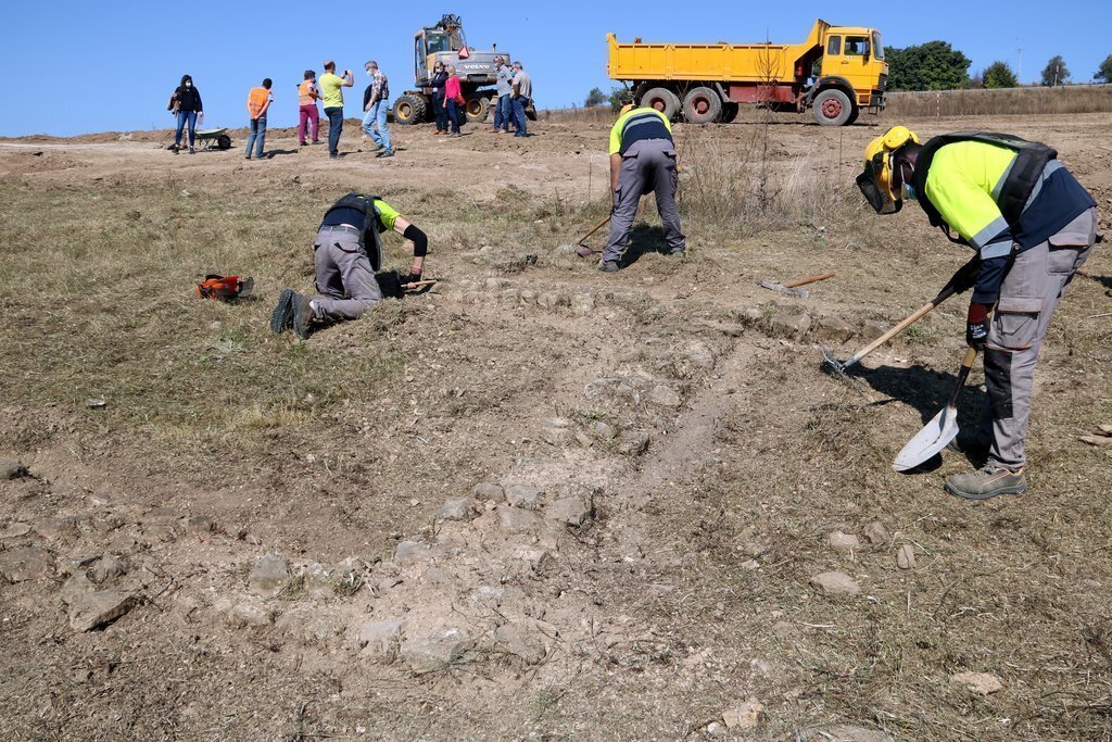 Un operari treballant al jaciment de la vil·la romana de Llorís i els arqueòlegs al fons explicant el que s'ha trobat de moment. Imatge del 20 de setembre del 2020. (horitzontal)