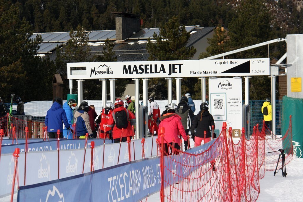 Pla obert on es veuen alguns esquiadors, d'esquena, accedint a la zona d'espera d'un dels remuntadors de l'estació de Masella (Cerdanya), en el primer dia de la temporada. Imatge del 14 de desembre de 2020 (Horitzontal).