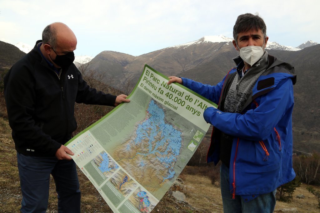 Pla mig de dos persones mostrant el pòster que ha editat el Parc Natural de l'Alt Pirineu sobre la glacera de la Noguera Pallaresa. Imatge del 5 de febrer del 2021. (horitzontal)