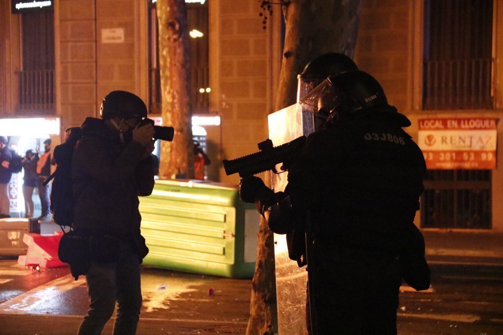 Un periodista fotografia uns agents dels Mossos d'Esquadra amb una llançadora de foam durant unes protestes per l'empresonament del cantant Pablo Hasel el 17 de febrer del 2021 a Barcelona. Pla general. (Horitzontal)