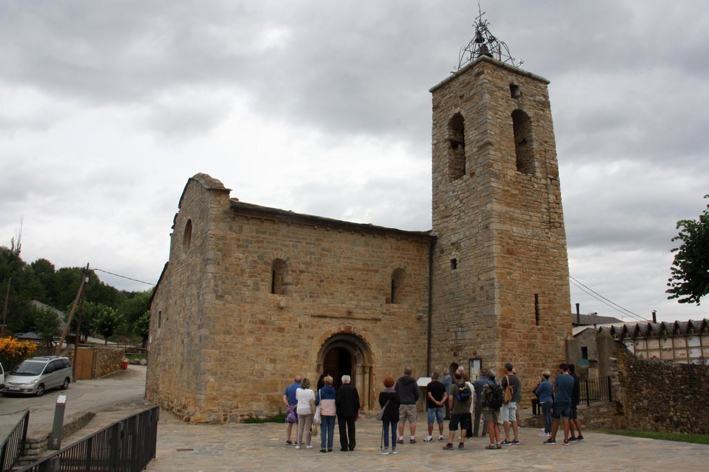Pla obert de l'exterior de l'església de Santa Maria d'All, a Isòvol (Cerdanya), on es pot veure un grup de visitants mirant la portalada. Imatge del 18 d'agost de 2020 (Horitzontal).