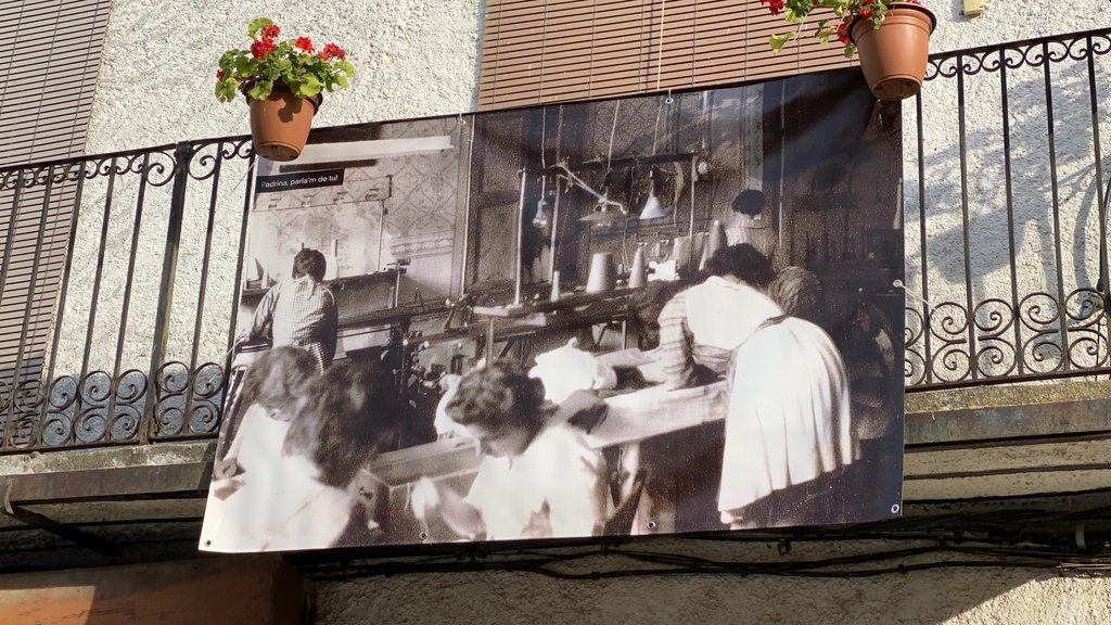 Pla de detall d'una pancarta amb una fotografia antiga col·locada en una façana d'una casa d'una plaça de Peramola (Alt Urgell) que forma part de la ruta de memòria històrica. Imatge del 19 d'agost de 2021. (Horitzontal)