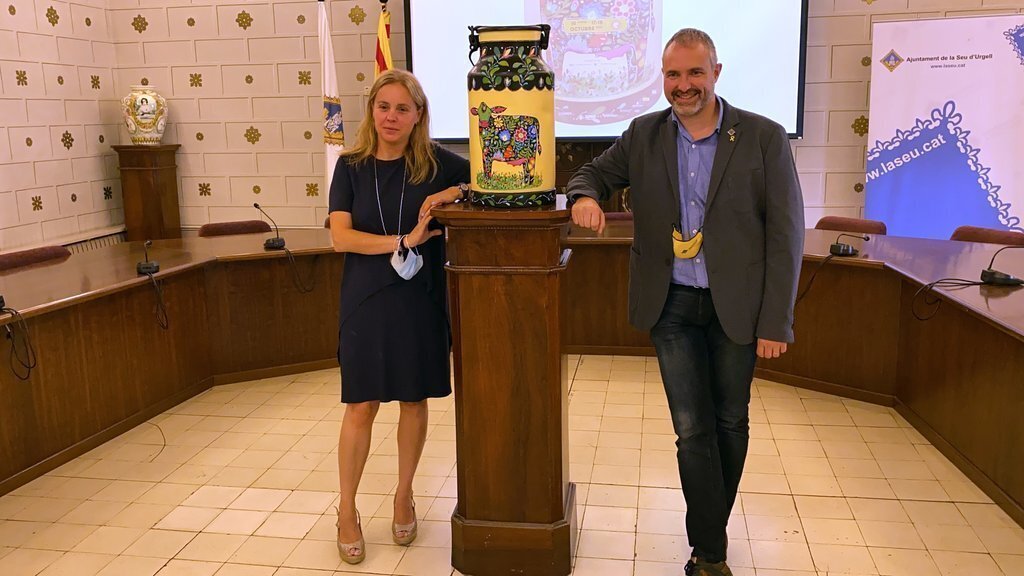 Pla sencer de l'alcalde de la Seu d'Urgell, Jordi Fàbrega, i la tinent d'alcalde de Promoció de la ciutat, Mireia Font, al costat d'una lletera amb la imatge de la Fira de Sant Ermengol d'enguany. Imatge del 2 de setembre de 2021. (Horitzontal)
