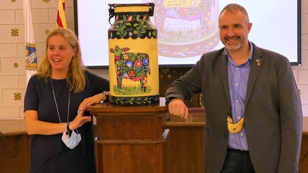Pla mitjà de l'alcalde de la Seu d'Urgell, Jordi Fàbrega, i la tinent d'alcalde de Promoció de la ciutat, Mireia Font, al costat d'una lletera amb la imatge de la Fira de Sant Ermengol d'enguany. Imatge del 2 de setembre de 2021. (Horitzontal)