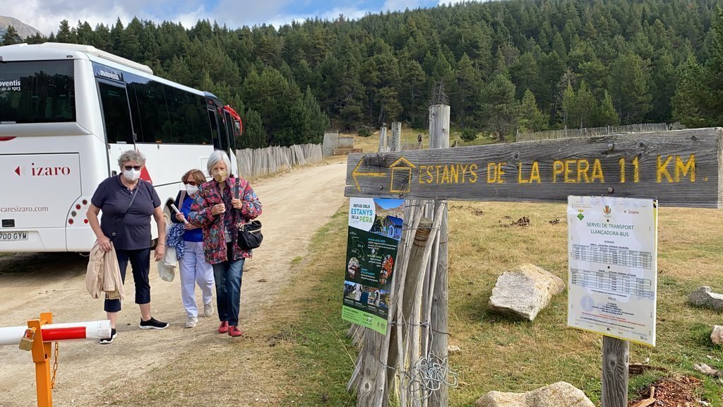 Pla obert on es veuen tres persones al costat d'un dels busos llançadora que cobreix el trajecte entre l'aparcament del Refugi Cap del Rec, a la base de l'estació de nòrdic de Lles, i la font de Pollineres. Imatge de l'1 de setembre de 2021. (Horitzontal)